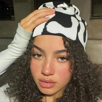 This image shows a woman wearing a black and white mea culpa beanie.